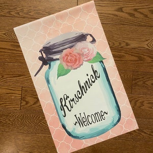 May include: A blue mason jar with a pink and white floral design and the text "Kirschnick -Welcome-" on a pink and white patterned background.