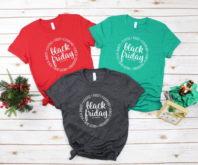 May include: Three t-shirts in red, green, and gray with a white circle design that says "COFFEE &bull; SALES &bull; COUPONS &bull; LUNCH &bull; SHOPPING &bull; MESSY BUN &bull; YOGA PANTS" around the words "black friday".