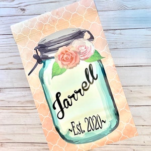 May include: A blue mason jar with a white lid and a floral design. The jar has the text "Farrell ~Est. 2020~" written on it.