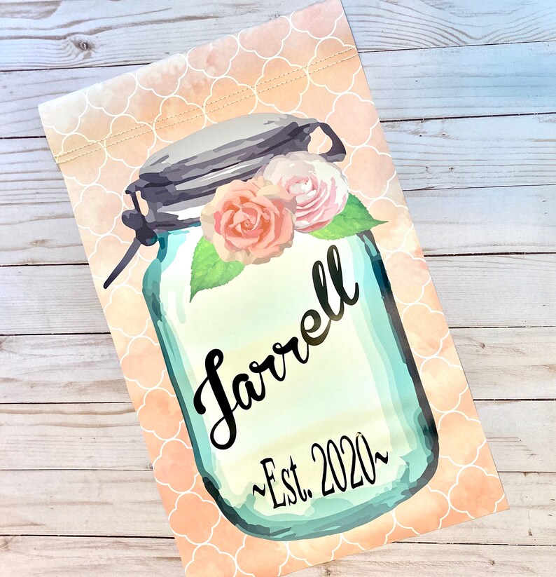 May include: A blue mason jar with a white lid and a floral design. The jar has the text "Farrell ~Est. 2020~" written on it.