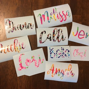 Op de afbeelding: Een verzameling gepersonaliseerde naamstickers in diverse kleuren en patronen. Elke sticker toont een andere naam, zoals "Melissa", "Diana" en "Calli", in een sierlijk lettertype. De ontwerpen bevatten bloemen en abstracte patronen.
