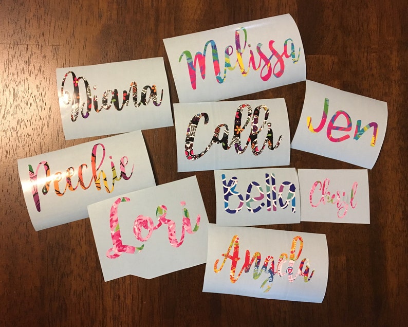 Op de afbeelding: Een verzameling gepersonaliseerde naamstickers in diverse kleuren en patronen. Elke sticker toont een andere naam, zoals "Melissa", "Diana" en "Calli", in een sierlijk lettertype. De ontwerpen bevatten bloemen en abstracte patronen.