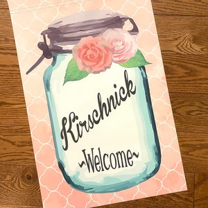 May include: A blue mason jar with a white background and pink flowers on top. The jar has the text "Kirschnick" and "Welcome" written on it. The background is a pink and white pattern.