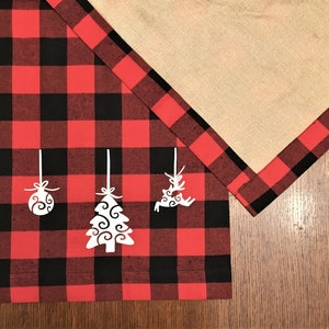 Puede incluir: Un camino de mesa de cuadros rojos y negros con adornos navideños recortados en blanco, incluyendo un árbol, un reno y una bola.