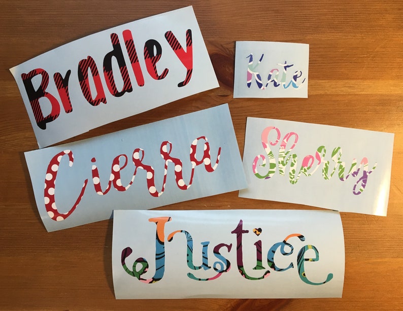 Op de afbeelding: Een verzameling gepersonaliseerde naamstickers in verschillende lettertypen en patronen. De namen zijn onder meer "Bradley" in rood en zwart geruit, "Kate" in pastelkleuren, "Cierra" met rode stippen, "Sherry" met bloempatronen en "Justice" in een kleurrijk ontwerp.