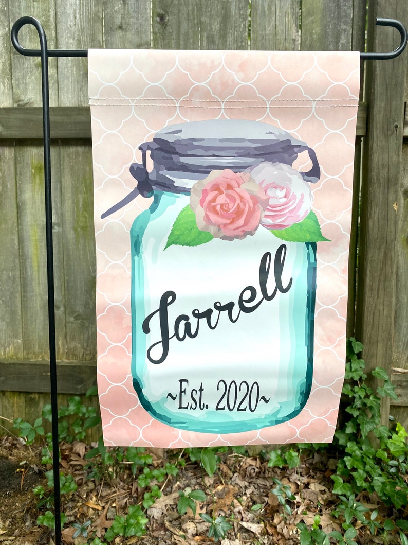 May include: A pink and white patterned garden flag with a blue mason jar with a gray lid and a floral design. The jar has the text "Farrell ~Est. 2020~" on it.