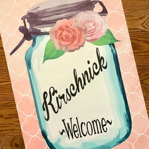 May include: A blue mason jar with a pink and white floral design and the text "Kirschnick -Welcome-" on a pink background with a white geometric pattern.