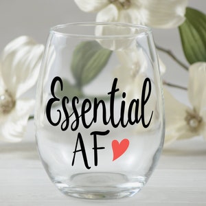 May include: A clear glass wine glass with the text "Essential AF" in black lettering and a red heart.