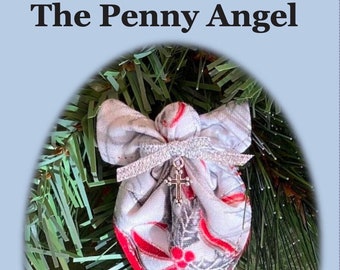 May include: A white fabric angel ornament with red and silver accents, hanging on a green artificial Christmas tree. The angel has a small pocket and a cross charm. The text "The Penny Angel" is at the top of the image. The text below the image reads "Stitch a penny angel from charm squares or quilt scraps. Place a heartfelt message inside the pocket with a penny and spread message of kindness throughout the year!"