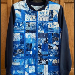May include: A blue and white quilted jacket with a zipper closure. The jacket is made of a patchwork of different blue and white fabrics, each with a unique pattern. The jacket has a navy blue collar and cuffs.