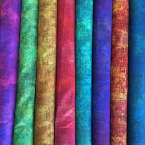 May include: Eight vertical rolls of fabric arranged side by side, each featuring a distinct mottled, textured pattern. The colors include purple, green, gold, red, teal, dark blue, orange-red, and deep blue, creating a vibrant spectrum.