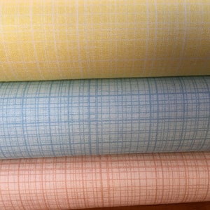 May include: Three rolls of fabric with a grid pattern. The top roll is yellow, the middle roll is light blue, and the bottom roll is peach.