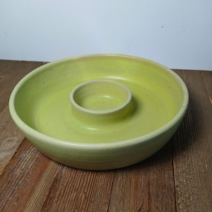 May include: A handmade, light green ceramic serving bowl with a central dip bowl. The bowl has a wide, shallow design with a smooth, glossy finish. The bowl is perfect for serving snacks or appetizers at a gathering.
