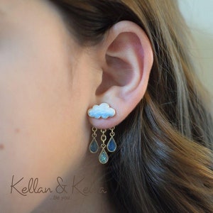 Puede incluir: Pendientes de botón con forma de nube con colgantes de gotas de lluvia. Los pendientes presentan un marco dorado con un diseño de nube blanca y azul claro. Tres colgantes en forma de lágrima cuelgan debajo, con detalles en azul y turquesa.