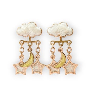 May include: Gold tone earrings with a white cloud charm and dangling stars and crescent moons. The stars have glitter accents.