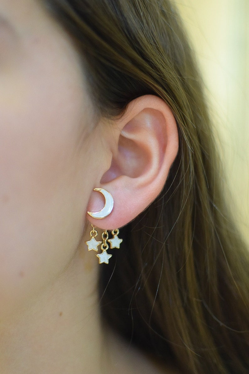 Model showcasing a pair of unique front-back earrings featuring a pearl white crescent moon at the front and three dangling stars at the back. These hypoallergenic earrings add a fun, starry night theme to any outfit.