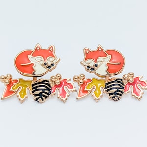 Close-up view of hand-painted, hypoallergenic red fox front back earrings with a sleeping orange fox and branch with orange and yellow leaves.