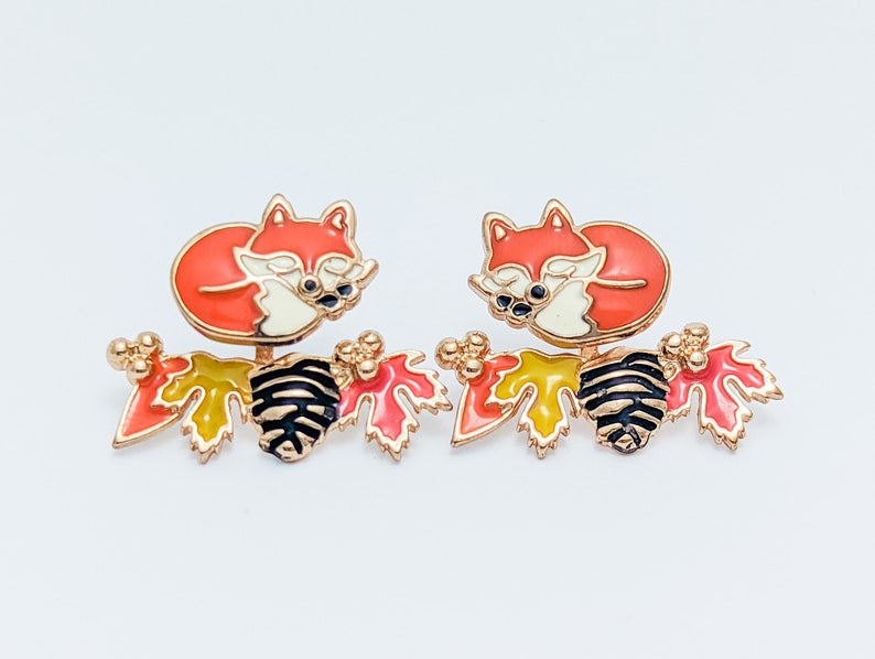 Close-up view of hand-painted, hypoallergenic red fox front back earrings with a sleeping orange fox and branch with orange and yellow leaves.