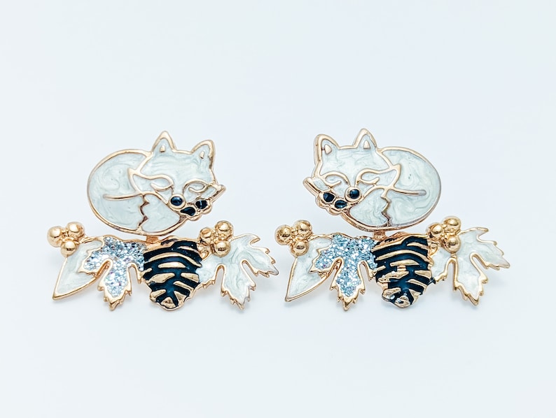 Close-up view of the winter version of the white fox front back earrings, featuring a sleeping white fox and branch with glittery white leaves."