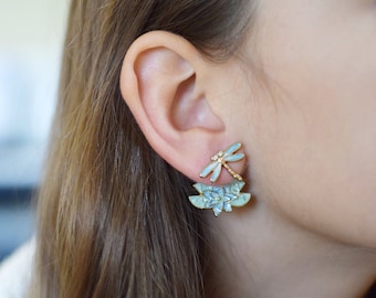 May include: A pair of gold earrings with a dragonfly design and a flower design. The dragonfly is blue and white with clear rhinestones. The flower is blue and white with a gold center.