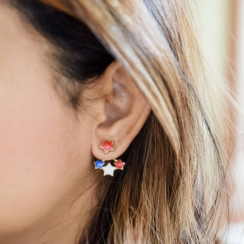 Independence Day-themed earrings modeled, highlighting the red and blue star studs with three colorful star ear jackets