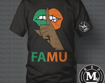 May include: Black t-shirt with a green and orange lips design and a finger over the lips. The text "FAMU" is written in green and orange letters below the lips. The shirt has a logo on the right side that says "Rep My School" with a logo of a white "M" inside a circle.