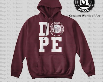 Op de afbeelding: Een bordeauxrode hoodie met een witte "DOPE"-afbeelding en een rond logo met de tekst "Texas Southern University" in wit en een bordeauxrode silhouet van een gebouw. Het logo is gecentreerd op de "O" van "DOPE".
