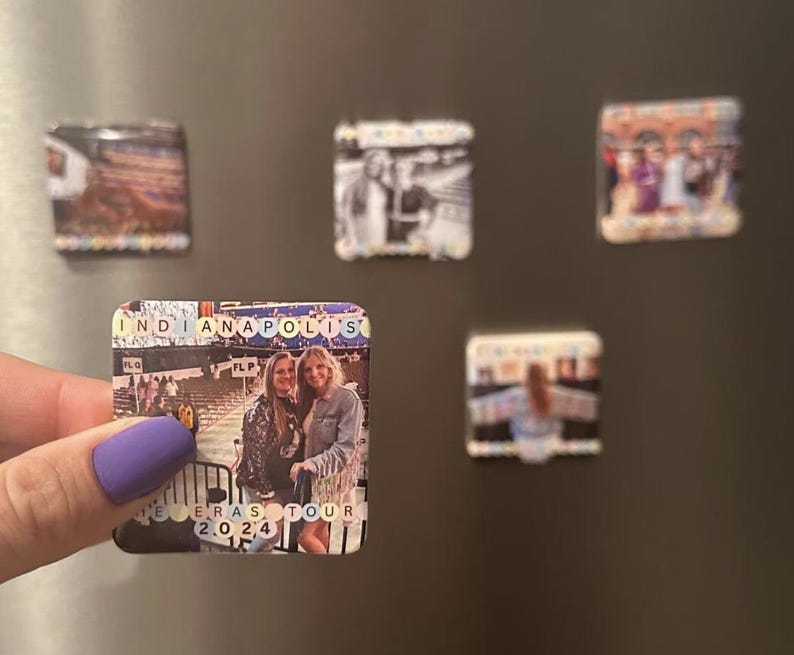 May include: A square magnet with a photo of two women standing in front of a building. The magnet has the text "INDIANAPOLIS" and "ERAS TOUR 2024" on it.