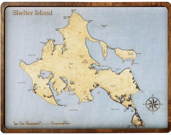 Op de afbeelding: Houten kaart van Shelter Island met een lichtblauwe achtergrond en een donkerbruine lijst. De kaart toont de topografie en geografische kenmerken van het eiland, met de tekst "Shelter Island" bovenaan.