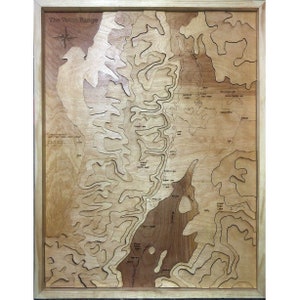May include: A wooden map of the Teton Range in Wyoming, with a compass rose and the words "The Teton Range" at the top. The map shows the major lakes and rivers in the area, including Jackson Lake, Jenny Lake, and the Snake River. The map is made of light wood with a dark wood frame.