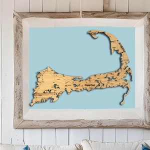 May include: A wooden map of Cape Cod, with detailed roads and waterways, is framed in a light wood frame and displayed on a white wall.
