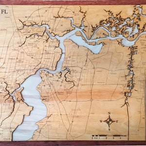 May include: A wooden map of Jacksonville, Florida, with a compass and scale in miles. The map is laser-cut and features the city's waterways and roads.