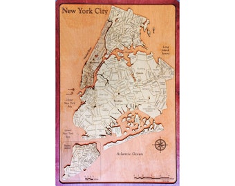 Op de afbeelding: Een houten kaart van New York City met de stadsdelen Manhattan, Brooklyn, Queens, The Bronx en Staten Island. De kaart bevat de namen van veel wijken en bezienswaardigheden. De kaart is omgeven door een rode houten lijst.