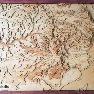 May include: A wooden map of the Catskill Mountains in New York State. The map is laser cut and shows the topography of the region. The map is framed in a dark wood frame.