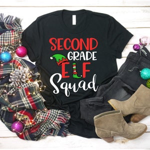 May include: Black t-shirt with white text that reads "Second Grade Elf Squad". The text is decorated with a green elf hat with red trim and a red and white striped elf shoe.