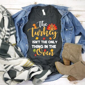 May include: A dark gray t-shirt with the text "The turkey isn't the only thing in the oven" and a cartoon turkey with fall leaves.