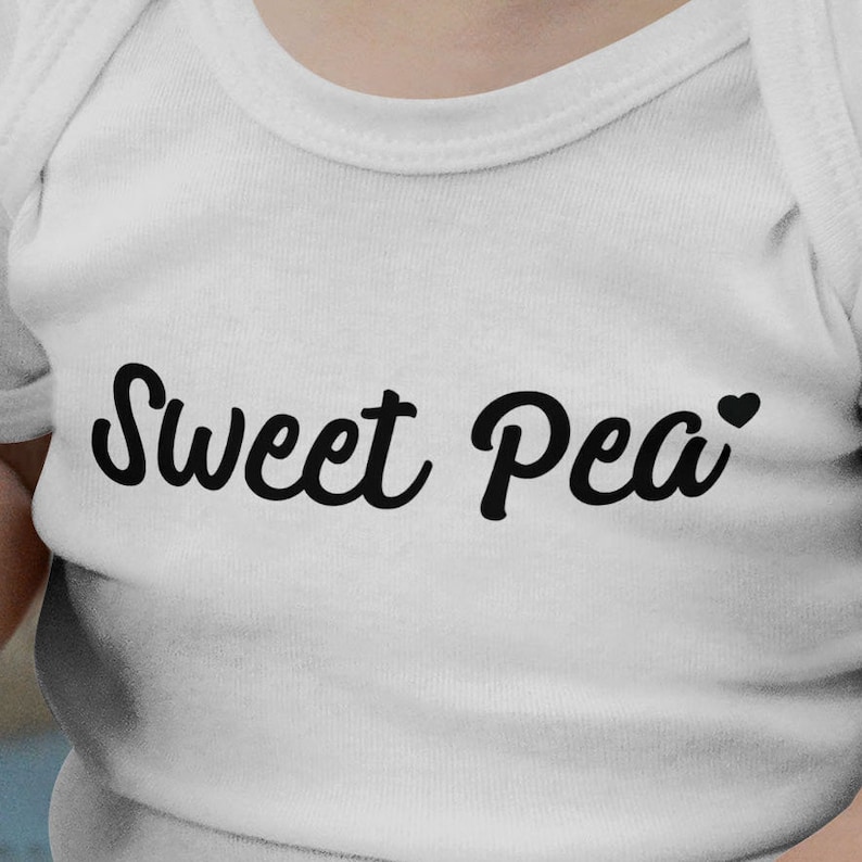 Może przedstawiać: Białe body dla niemowląt z napisem "Sweet Pea" czarną, kursywą. Małe czarne serce znajduje się obok słowa "Pea". Body wykonane jest z miękkiej, białej tkaniny.