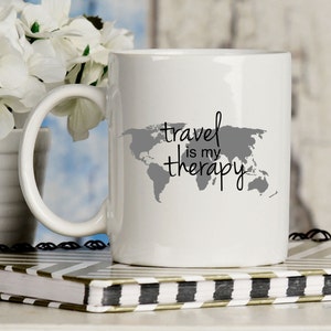 May include: White ceramic mug with a gray world map and the text "travel is my therapy" in black.