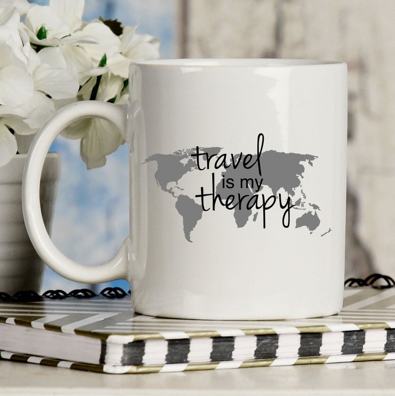 May include: White ceramic mug with a gray world map and the text "travel is my therapy" in black.