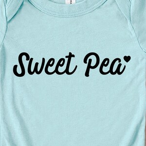Może przedstawiać: Jasnoniebieskie body dla dziecka z napisem "Sweet Pea" czcionką w kolorze czarnym. Małe czarne serce znajduje się obok słowa "Pea". Body jest wykonane z miękkiego materiału.
