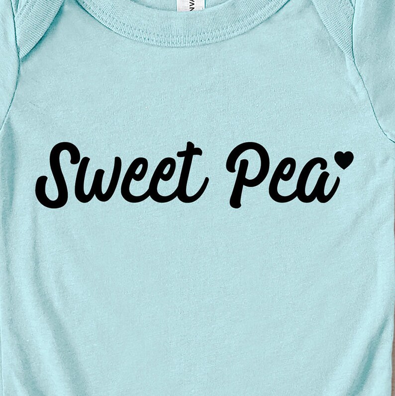 Może przedstawiać: Jasnoniebieskie body dla dziecka z napisem "Sweet Pea" czcionką w kolorze czarnym. Małe czarne serce znajduje się obok słowa "Pea". Body jest wykonane z miękkiego materiału.