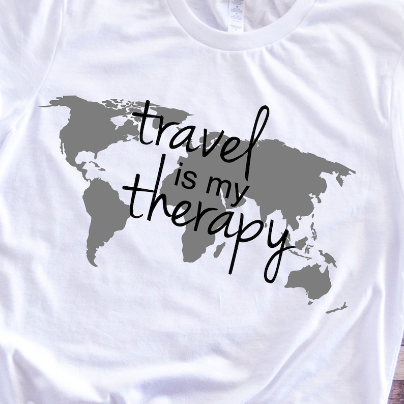 May include: White t-shirt with a gray world map graphic and the text "travel is my therapy" in black.
