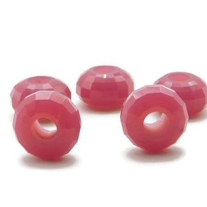 Könnte beinhalten: Fünf rosafarbene, facettierte Glasperlen mit einem Loch in der Mitte. Die Perlen sind in einem Halbkreis auf weißem Hintergrund angeordnet.