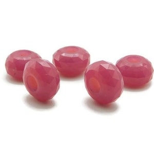 May include: Five pink faceted glass beads with a hole in the center. The beads are round and have a shiny finish.