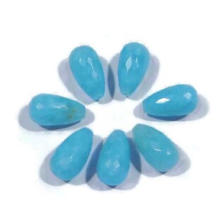 May include: Seven teardrop-shaped turquoise beads, each with a faceted surface, arranged in a circle on a white background.