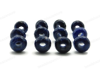 May include: A close-up of twelve dark blue faceted gemstone beads. The beads are round and have a hole in the center. The beads are arranged in a row on a white surface.