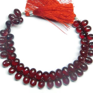 May include: A strand of deep red gemstone beads, likely garnet, with a faceted oval shape. The beads are strung on a cord with a red tassel at the end.