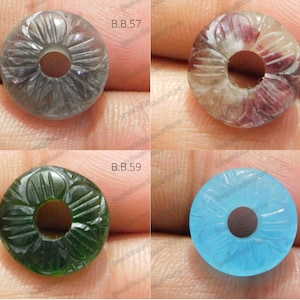 May include: Four carved gemstone beads with a hole in the center. The beads are in shades of gray, purple, green, and blue.