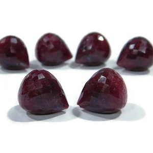 Op de afbeelding: Zes gefacetteerde, druppelvormige edelstenen in verschillende maten. De edelstenen hebben een diepe, rijke bordeauxrode kleur, met een gepolijst, reflecterend oppervlak. Ze zijn gerangschikt op een witte achtergrond.