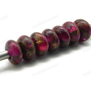 Puede incluir: Una hebra de siete cuentas redondas, rosadas y doradas con un brillo metálico. Las cuentas están enhebradas en un alambre plateado.